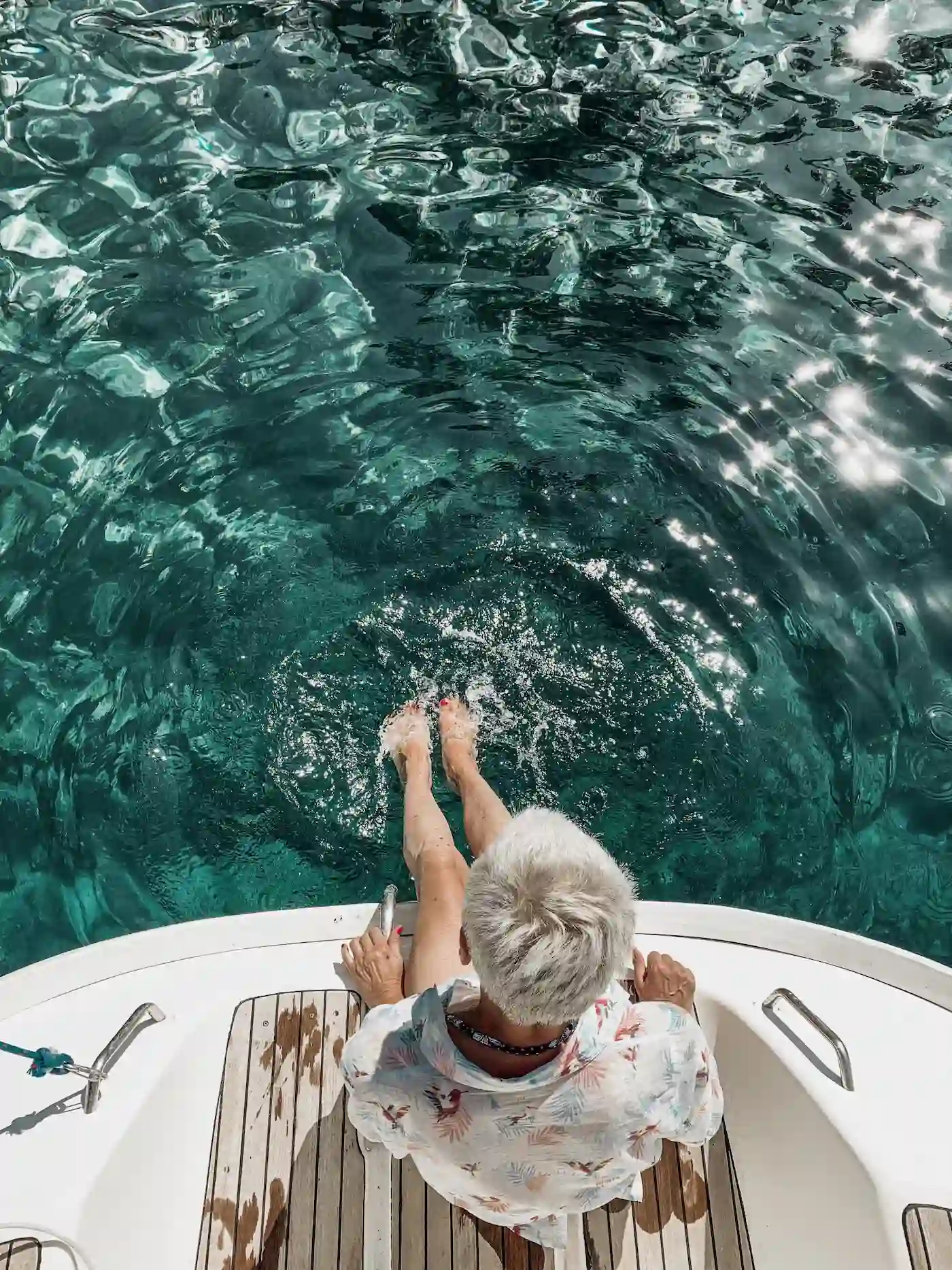 Person relaxing on a boat with legs in sparkling turquoise water.